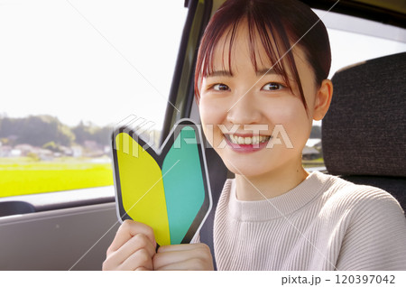 運転席で初心者マークを持つ笑顔の女性 120397042
