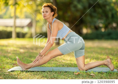 Woman practicing yoga in garden, performing Anjaneyasana, or Crescent Moon Pose 120398095