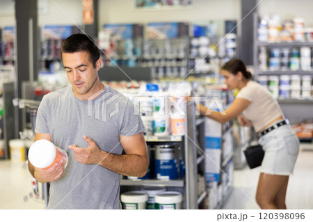 Man buys tin with paint in paintwork material store for carrying out internal finishing work on object 120398096