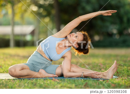 Woman practicing hatha yoga in garden, stretching in an asymmetrical seated asana Parivritta Janu Sirsasana 120398108