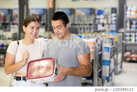 Husband buyer with paint container in hand consults with wife and examines can of enamel dye Husband buyer with paint container in hand consults with wife and examines can of enamel dye 120398111