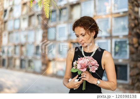 Woman in black mourning dress standing with flowers near columbarium 120398138