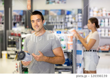 Man buys tin with paint in paintwork material store for carrying out internal finishing work on object Man buys tin with paint in paintwork material store for carrying out internal finishing work on object 120398139