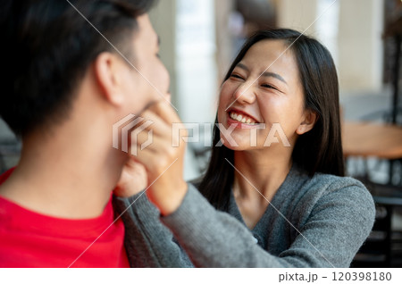 The girlfriend is playfully pinching her boyfriend's face, expressing love and cuteness. 120398180
