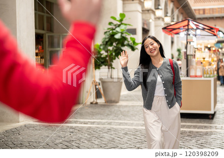 A happy Asian woman is waving at her friend to say hi, after an unexpected meeting in the city. 120398209