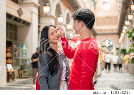 A caring young Asian boyfriend is adjusting his girlfriend's hair while they shop together at a mall 120398215