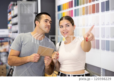 Positive couple talking while choosing paints and tools in store Positive couple talking while choosing paints and tools in store 120398229