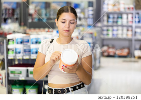 Interested young woman reading label on paint cans in hardware store 120398251