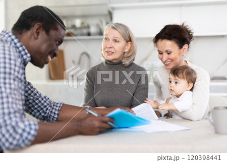 Two women with baby sitting at the kitchen-table face to face with male agent Two women with baby sitting at the kitchen-table face to face with male agent 120398441