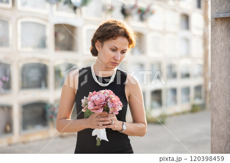 Woman in black mourning dress standing with flowers near columbarium 120398459