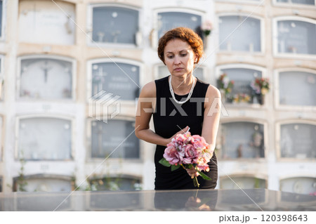 Grieving woman in black placing bouquet on grave Grieving woman in black placing bouquet on grave 120398643