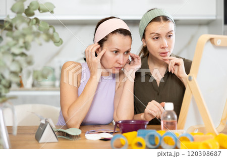 Two adult besties inspecting faces in mirror in cozy home 120398687