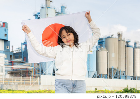 Happy young woman with flag of Japan against background of factory 120398879
