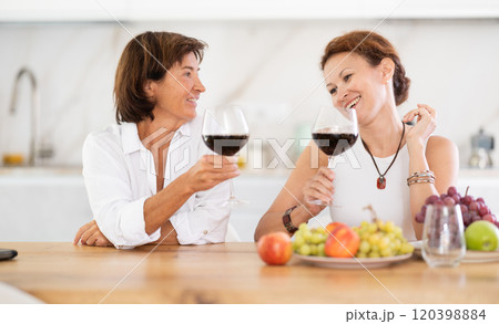Two girlfriends chatting and drinking red wine in cozy home kitchen 120398884
