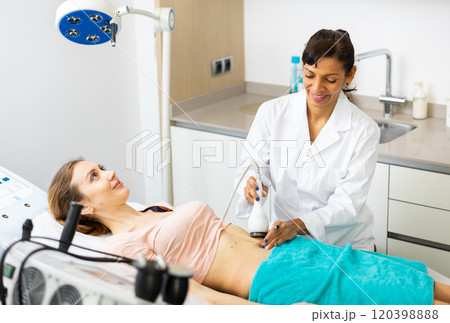 Beautician doing ultrasound lifting procedure in woman's abdominal region Beautician doing ultrasound lifting procedure in woman's abdominal region 120398888