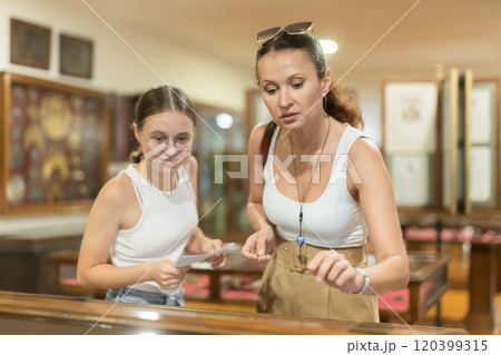 Young woman with teen daughter visitors stands near horizontal glass display case Young woman with teen daughter visitors stands near horizontal glass display case 120399315