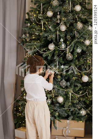 A young boy is decorating a Christmas tree with ornaments A young boy is decorating a Christmas tree with ornaments 120399524