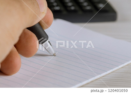 Hand grips a pen over blank lined paper, ready to write calculator is visible in background, suggesting focus on tasks productivity. 120401050