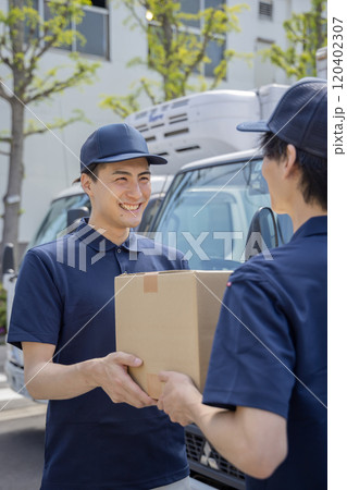 担当地域の配達員に荷物を渡す同僚 120402307
