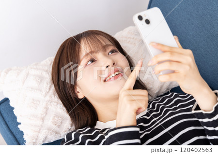ソファーでスマホを寝そべりながら使う女性 ソファーでスマホを寝そべりながら使う女性 120402563