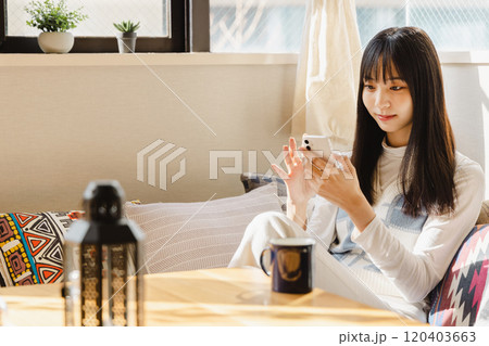 ローソファーに座りスマートフォンを使う若い女性 120403663
