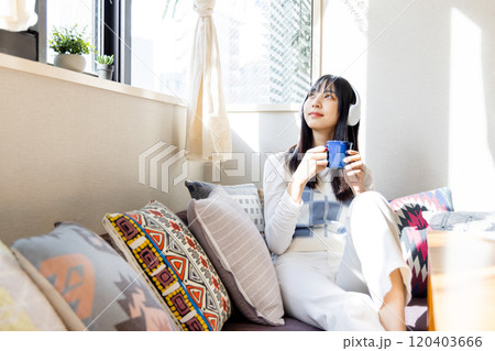 ローソファーに座りスマートフォンで音楽を聴く若い女性 120403666