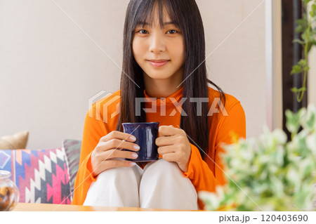 膝を立てコーヒー・紅茶を飲む若い女性 120403690