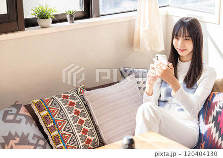 ローソファーに座りスマートフォンを使う若い女性 120404130