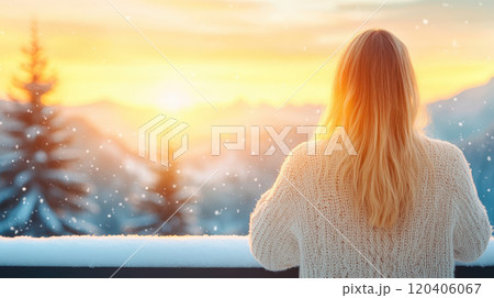 woman with long hair stands on balcony, gazing at beautiful sunset over snowy mountains. scene is serene, with snowflakes gently falling around her 120406067