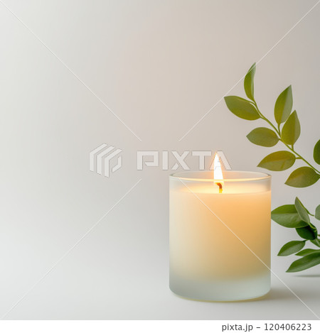 decorative scented candle in frosted glass holder, glowing softly. calming ambiance is enhanced by green leaf nearby, creating serene atmosphere 120406223
