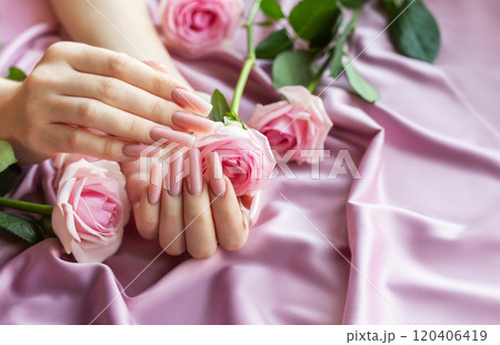 Woman showing pink manicure holding pink roses on satin sheet 120406419