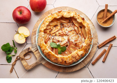 Homemade apple tart with almond toppings on a wooden board surrounded by fresh apples and cinnamon Homemade apple tart with almond toppings on a wooden board surrounded by fresh apples and cinnamon 120406423