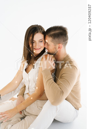 Young man and woman are sitting on a white surface, hugging each other. Scene is warm and affectionate Young man and woman are sitting on a white surface, hugging each other. Scene is warm and affectionate 120409287