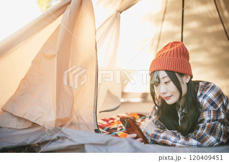 キャンプでテントに寝ながらスマホをいじる女性 キャンプでテントに寝ながらスマホをいじる女性 120409451
