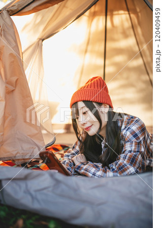 キャンプでテントに寝ながらスマホをいじる女性 120409459