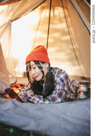 キャンプでテントに寝ながらスマホをいじる女性 キャンプでテントに寝ながらスマホをいじる女性 120409460