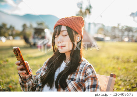 キャンプ場で座りながら音楽を聴く女性 キャンプ場で座りながら音楽を聴く女性 120409575