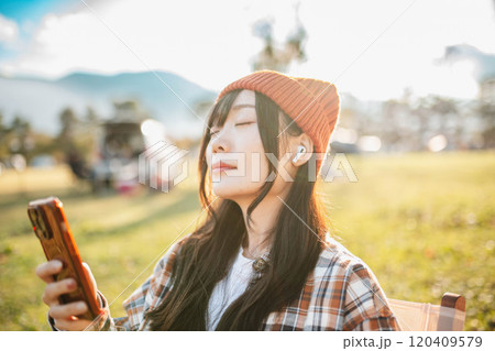 キャンプ場で座りながら音楽を聴く女性 120409579