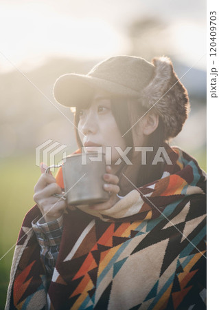 キャンプ場で毛布にくるまりながら飲み物を飲む女性 キャンプ場で毛布にくるまりながら飲み物を飲む女性 120409703