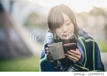 キャンプ場で毛布にくるまりながら飲み物を飲む女性 キャンプ場で毛布にくるまりながら飲み物を飲む女性 120409722