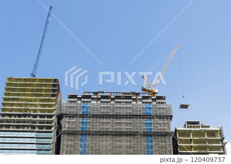 Low-angle view of cranes and steel structures of building construction with a blue sky background. Low-angle view of cranes and steel structures of building construction with a blue sky background. 120409737