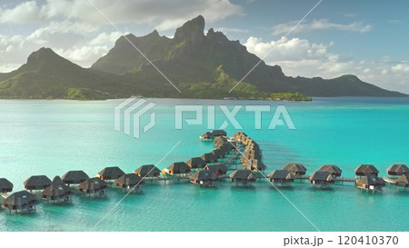 Aerial view overwater bungalows forming line towards mount Otemanu on tropical exotic Bora Bora island, with its turquoise lagoon and lush vegetation. Luxury travel vacation resort in coral reef ocean 120410370