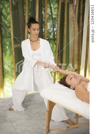 Beautiful female manual physician works with woman who lying on back on massage table in pro salon, vertical image, selective focus. 120416651