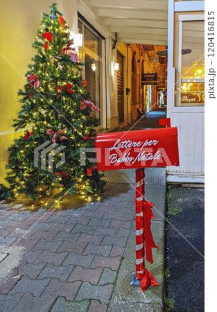 Red mailbox for Santa Claus letters near beautifully decorated Christmas tree with lights and bows. Lettere per Babbo Natale - Letters for Santa Claus 120416815