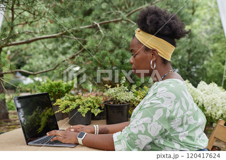 Side view portrait of young African American woman using laptop computer in green plantation and typing while managing eco theme small business Side view portrait of young African American woman using laptop computer in green plantation and typing while managing eco theme small business 120417624