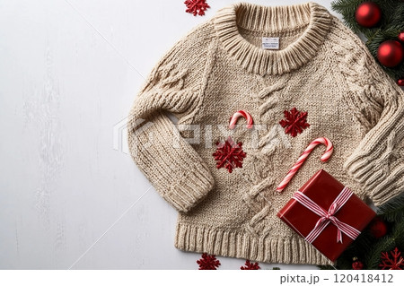 Top view of a warm knitted sweater with festive Christmas decorations, including candy canes, gift box, and red baubles Top view of a warm knitted sweater with festive Christmas decorations, including candy canes, gift box, and red baubles 120418412