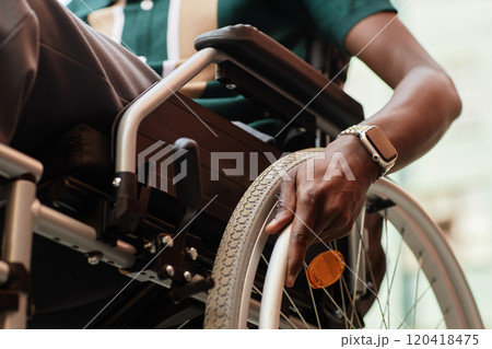 Detail shot of unrecognizable Black man with disability using wheelchair outdoors moving wheels, copy space 120418475