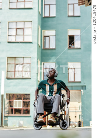 Vertical full length portrait of young Black man with disability wearing headphones and listening to music in city setting, copy space 120418479