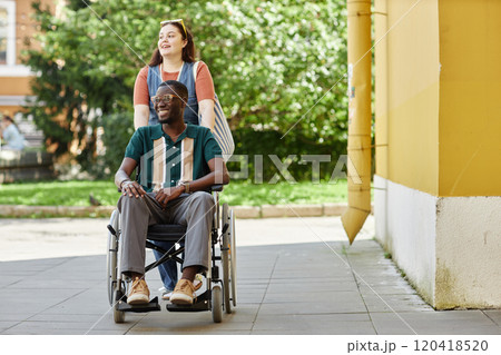 Vibrant full length portrait of smiling African American man with disability in city street with friend or partner assisting and moving towards camera copy space 120418520