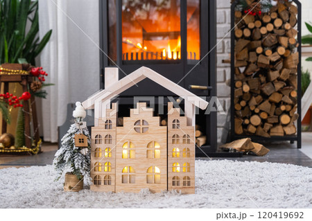 Key on Christmas tree and tiny house on cozy home with Christmas decor near the burning stove fireplace. Gift for New Year. Insurance, moving to new house, mortgage, rent and real estate 120419692